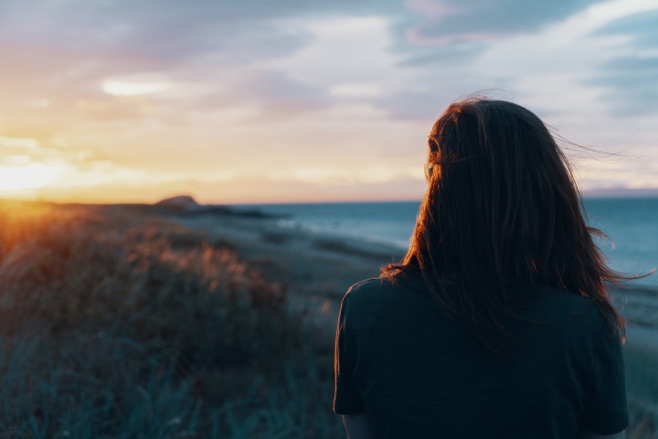 a woman standing with her back turned as she faces the sunset on the horizon