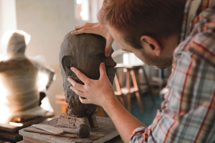 A sculpture forming a human head out of clay.