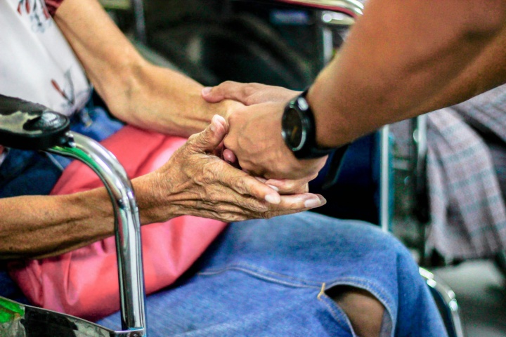 A man holding an older woman's hand sitting in a wheelchair. 