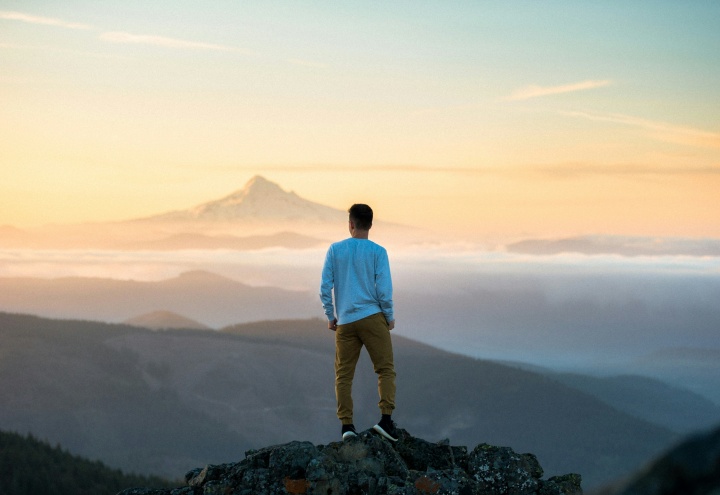 A young man standing on a rock looking out over a vista.