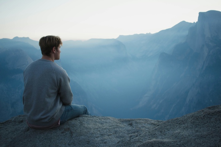 A young man sitting on rock looking out over a valley.