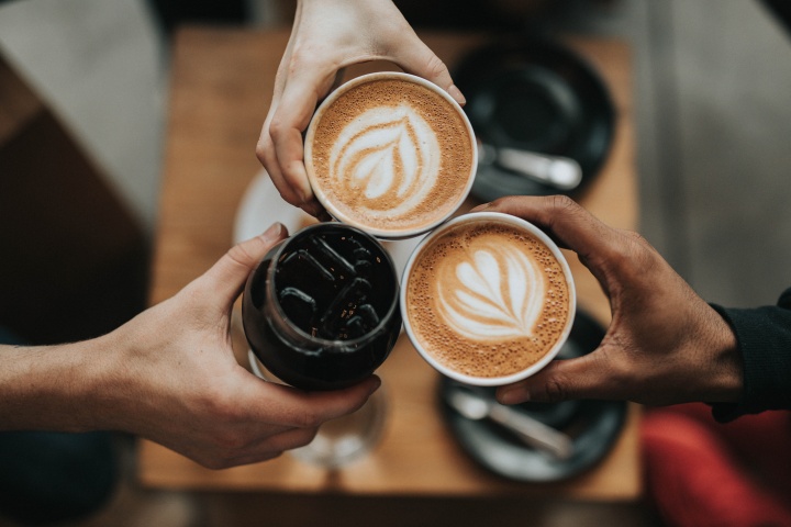 three hands, each holding a cup of coffee
