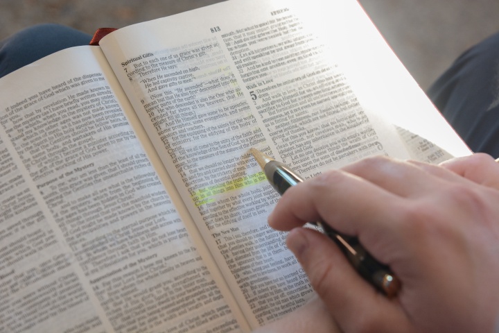 A photo of a hand highlighting a scripture in the Bible. 