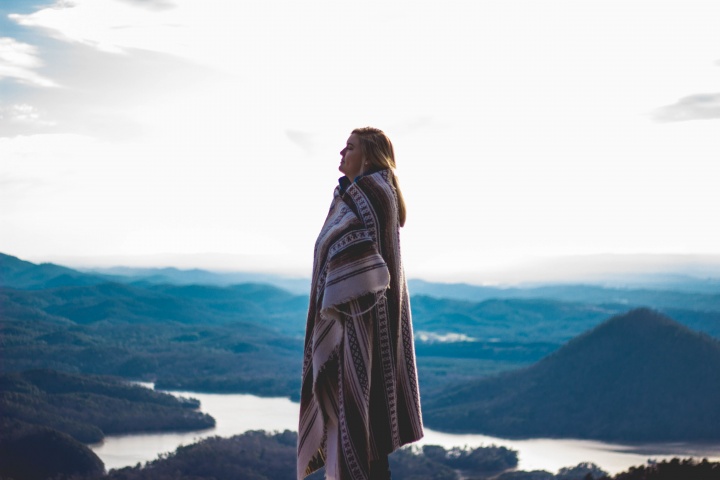 A woman wrapped in a blanket standing outside with mountains in the background.