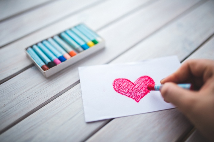 A person drawing a red heart with a crayon.