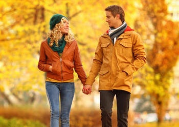 A man and woman holding hands walking in a park in the fall.