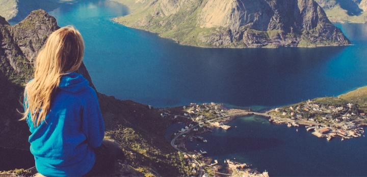 A young woman on top of a mountain looking at a lake.