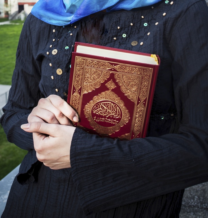 Woman holding a copy of the Quran in her arms.