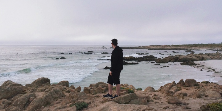 A man walking on a rocky shore of the ocean.