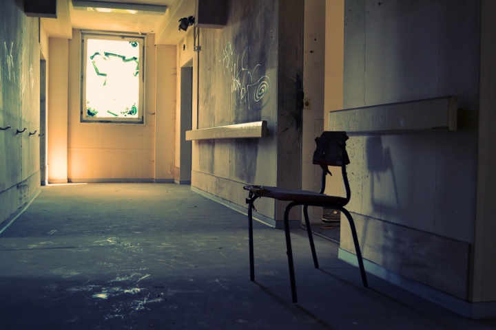 A lone student desk in a old run down school hallway.