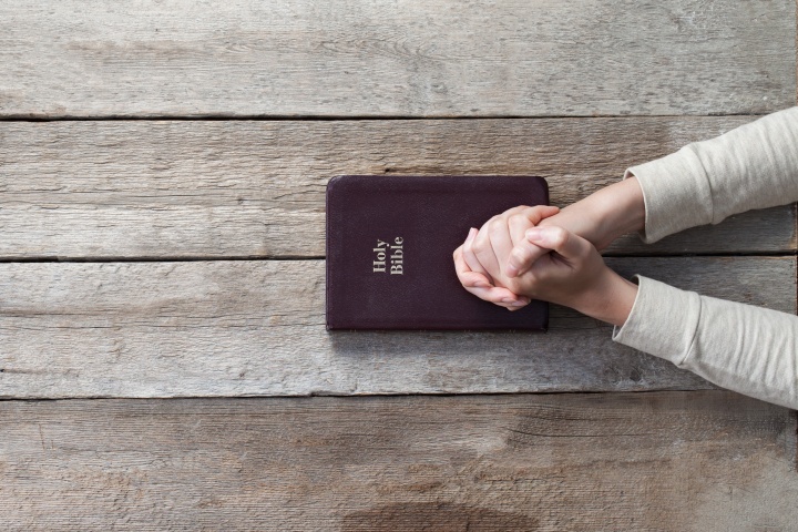 A person with their hands on top of a Bible that is on a table.