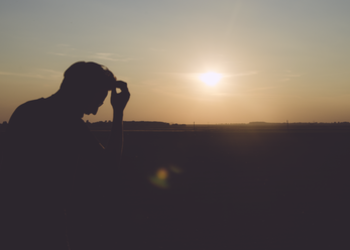 A man with head down as sun is setting.