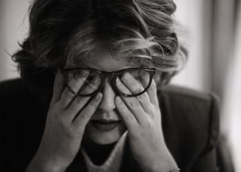 A woman wiping her eyes under her glasses.