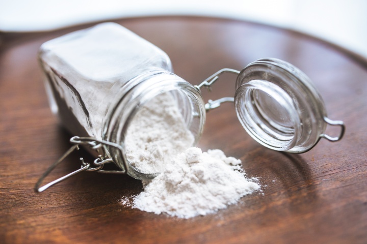 A glass jar of flour on its side with flour spilled out.