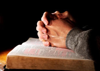 Hands clasped onto of a Bible as if person is praying.