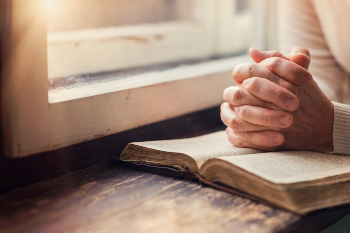 A woman reading a Bible by a window.