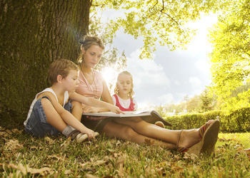 A mother reading to two children sitting outside.