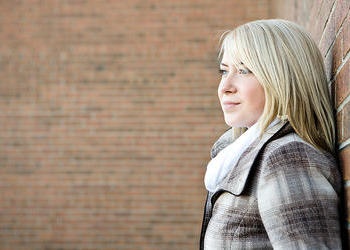 A teenage girl standing by a brickwall.