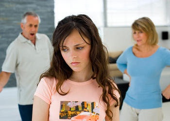 Teen girl in foreground with upset parents in background