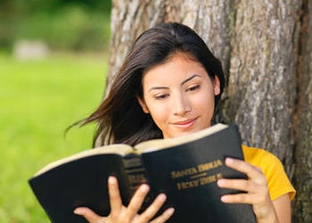 A young woman reading a Spanish version of the Bible (Santa Biblia).