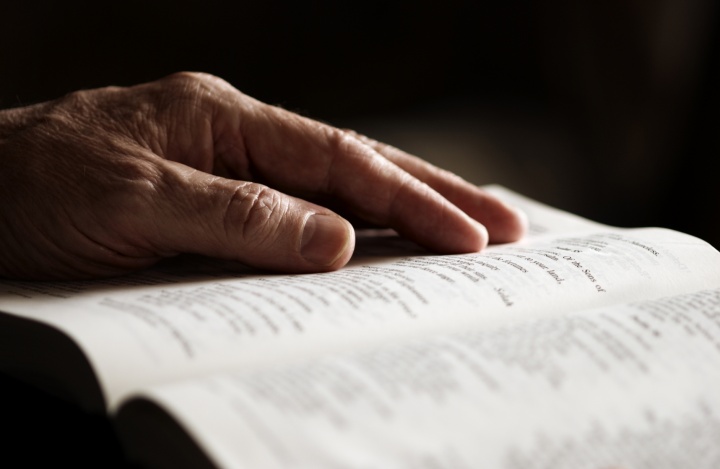An older man's hand on an open Bible.