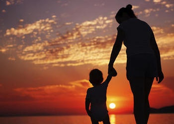 A mother holding her child's hand while watching the sun set.