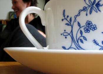 Close up tea cup with woman in background talking.