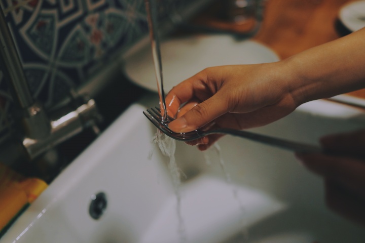 A woman washing a fork in a kitchen sink.
