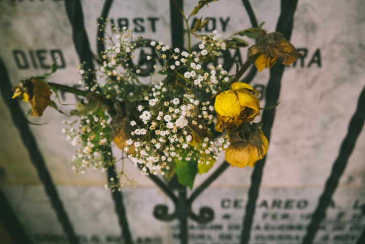 A tombstone with an iron fence and dried flowers in front of it.