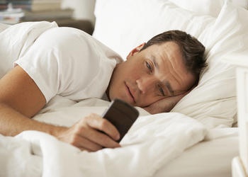 A man lying in bed staring at his smartphone.
