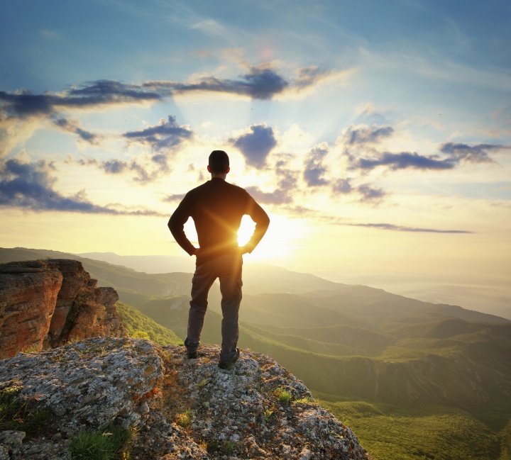 A young man on a cliff looking at the sunset.