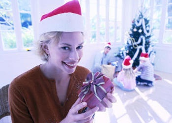 A young woman holding a small present in front of Christmas tree.