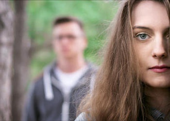 A young couple - woman in the foreground, man in the background blurred.