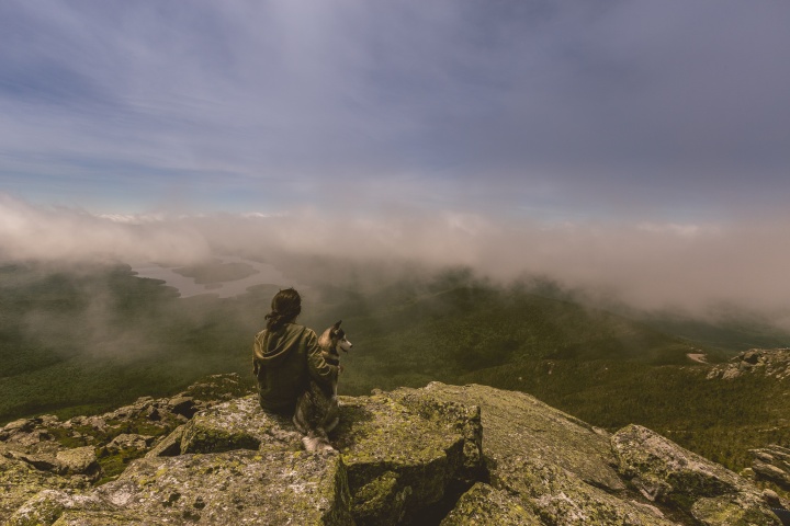 A woman sitting on cliff edge with her dog.