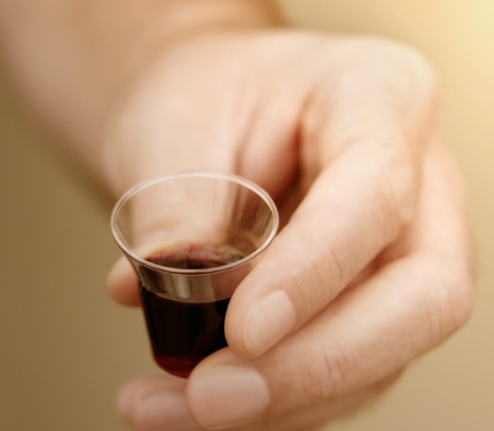 A man holding a small clear cup of wine.