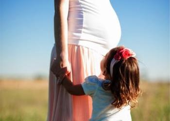 A young child holding a pregnant woman's hand.