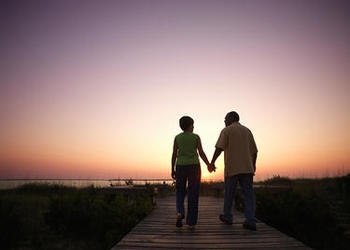An older couple walking on a board walk while sun is setting.