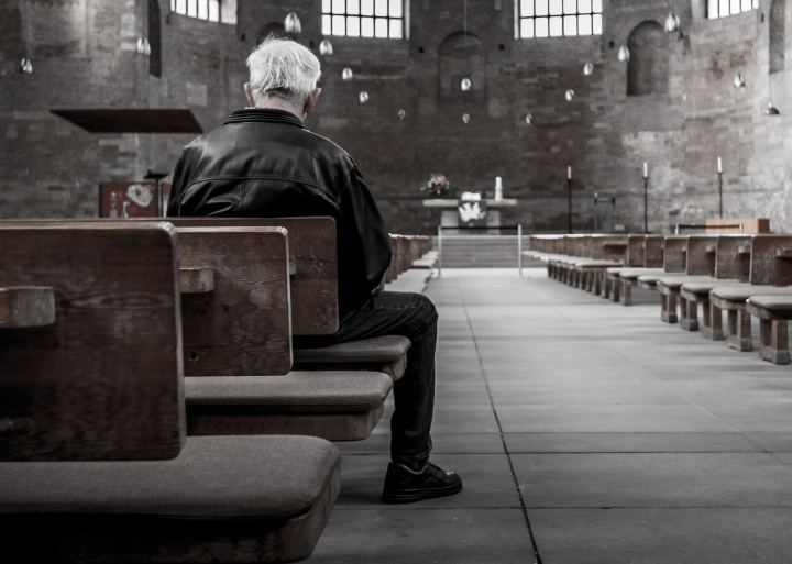 A old man sitting in a pew in an old church.