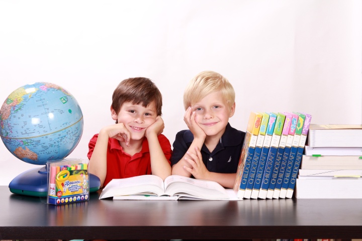 two boys with an open textbook on a desk alongside a globe and other school supplies