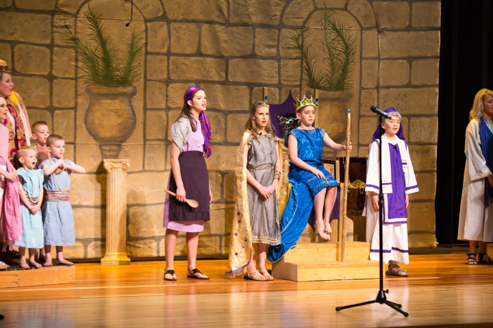 Right to left: the choir, Brooklyn Booth plays the narrator/palace cook, Cadence Phelps as Queen. Jedidiah, James Morris sits on his throne as Josiah, and Aaron Preston as Hilkiah. 