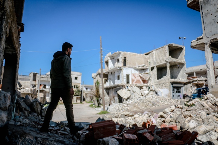 a man looks out over a pile of rubble and landscape of crumbled buildings