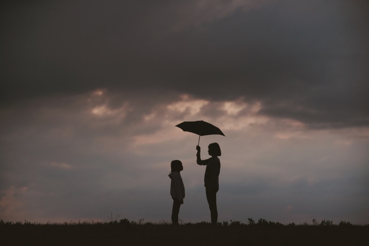 Photo of a girl holding an umbrella over another girl.