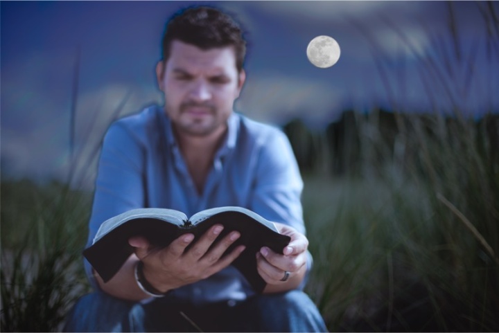 A man reading a Bible in the light of a full moon