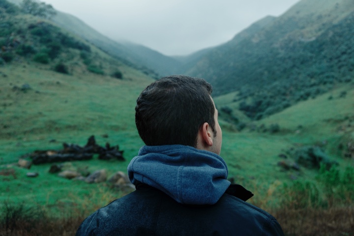 a man looks towards a mountain landscape that slopes up both to the right and to the left