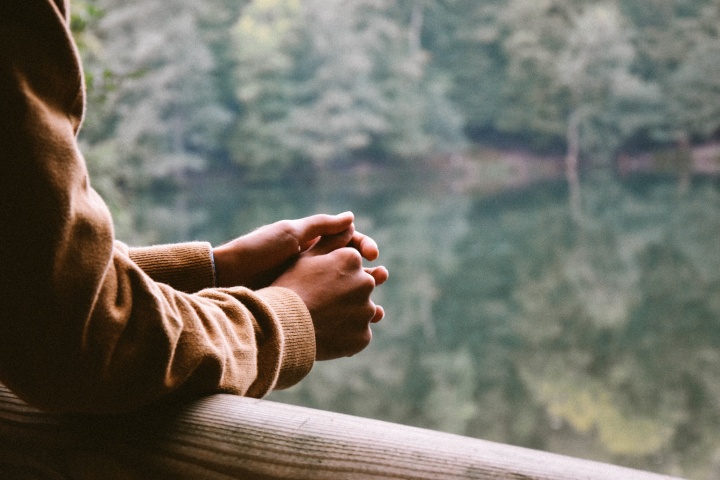 A man resting his arms on a railing looking over a lake.