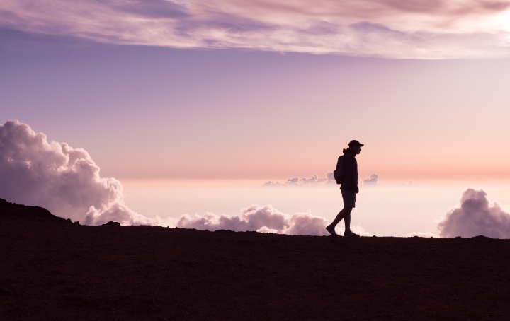 Photo of the the silhouette of a person walking against a sunset purple sky.