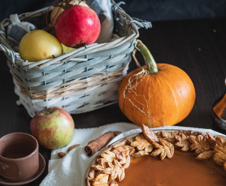 a basket of apples, pumpkin pie, coffee mug, and cinnamon stick