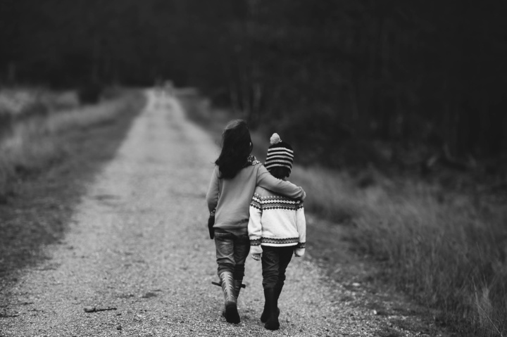 Black and white photo of two children walking down a road, each with an arm around the other's shoulders.