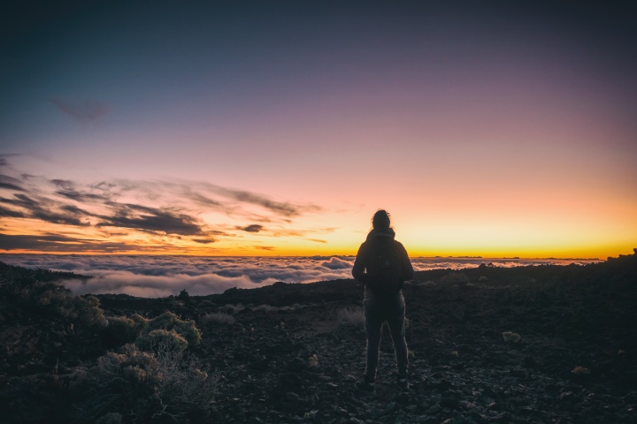 A woman on top of a mountain look out of over the clouds.