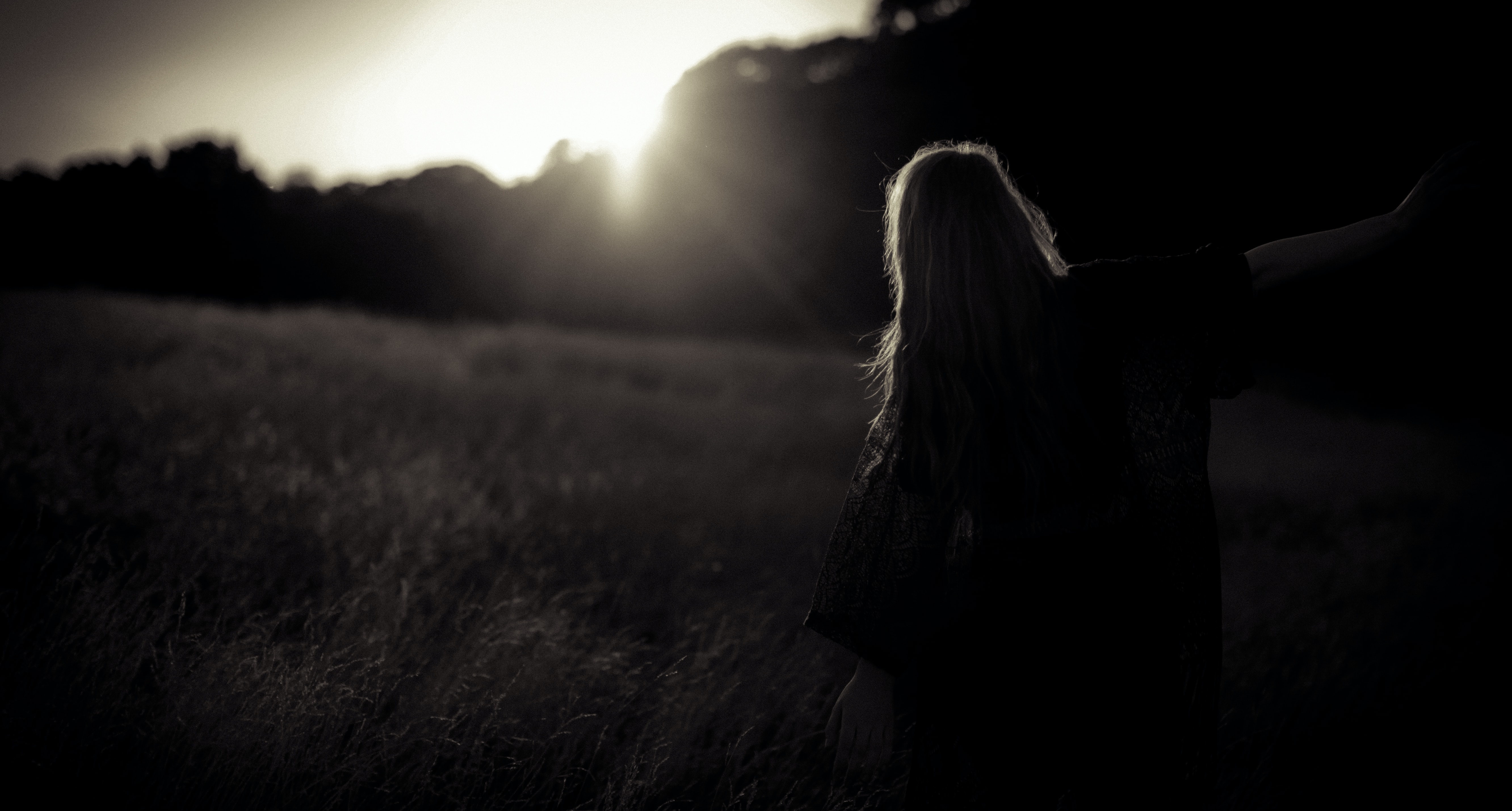 A woman sitting in a field while the sun is setting.